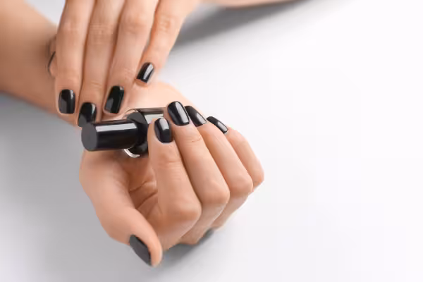 A woman's hands with black polished nails are holding a black polish jar
